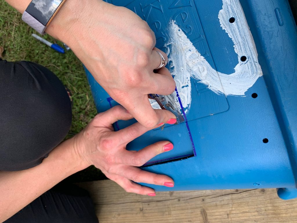 A photo of a sharp blade being used to cut a square out of a plastic storage container