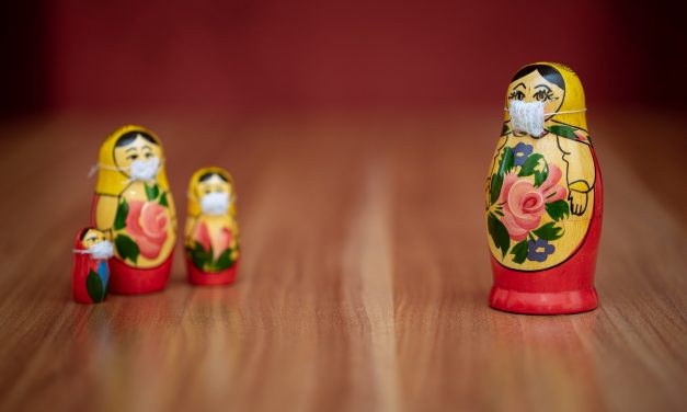 Four russian dolls wearing face coverings three standing together and one on its own