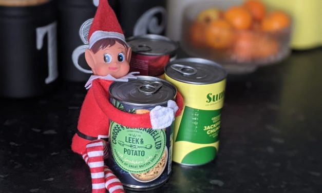 Elf of the shelf sits on kitchen counter hugging a tin of soup