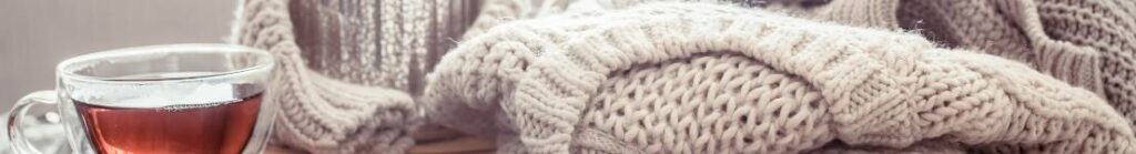 Close up divider image of some warm knitted blankets and a cup of tea in a c=glass teacup