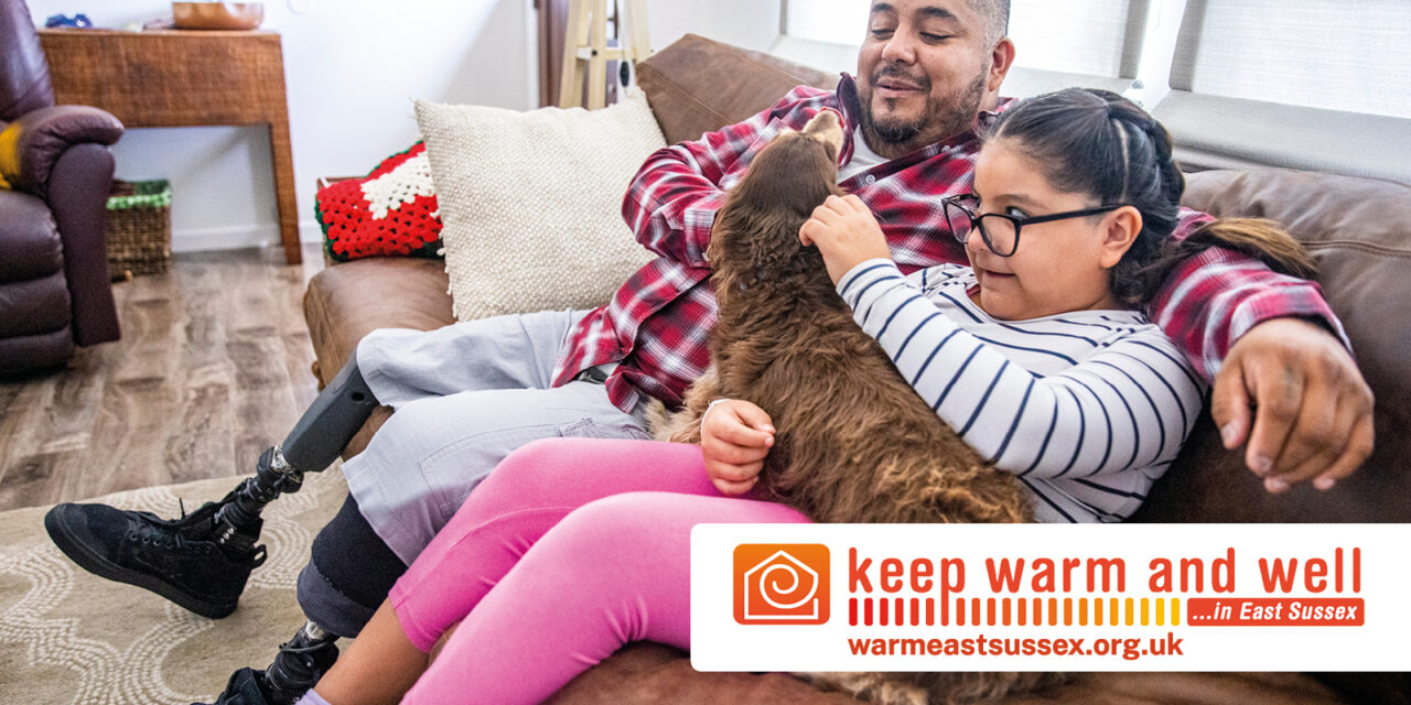 Parent and child with their dog at home. With the Keep Warm and Well logo.