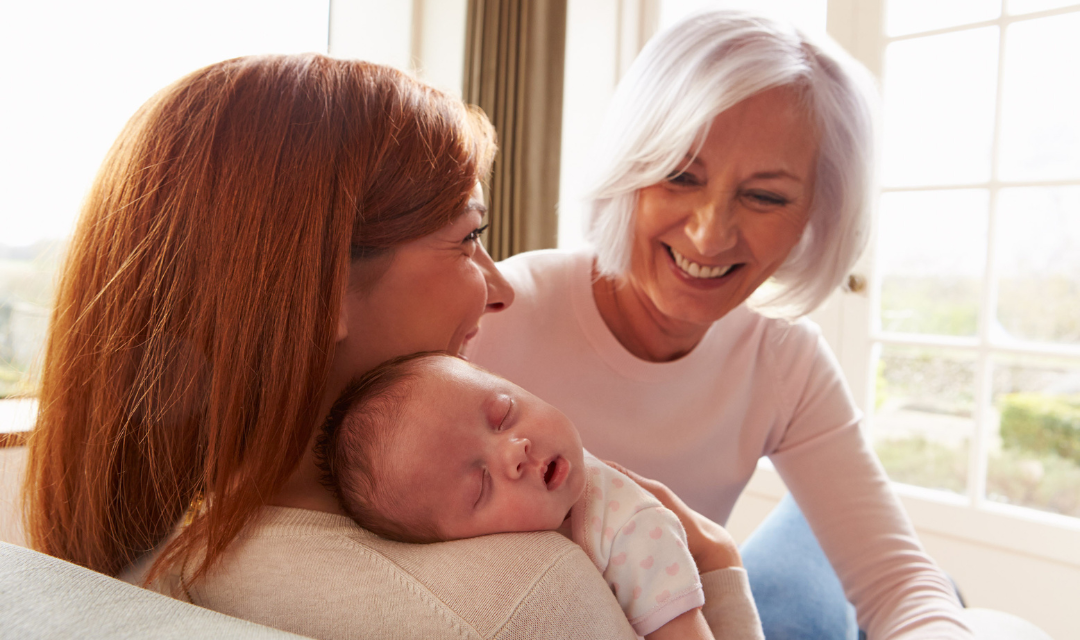 Two women holding a young baby and smiling