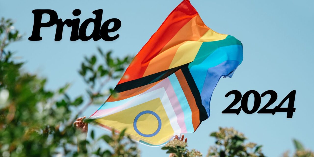 The pride flag with text reading: 'Pride 2024'. The photo is taken on a bright, sunny day with someone holding the flag in the wind.