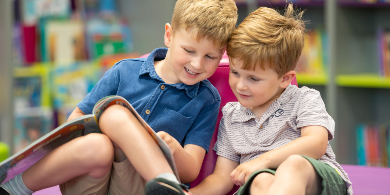 Two young boys reading a book together in a library.