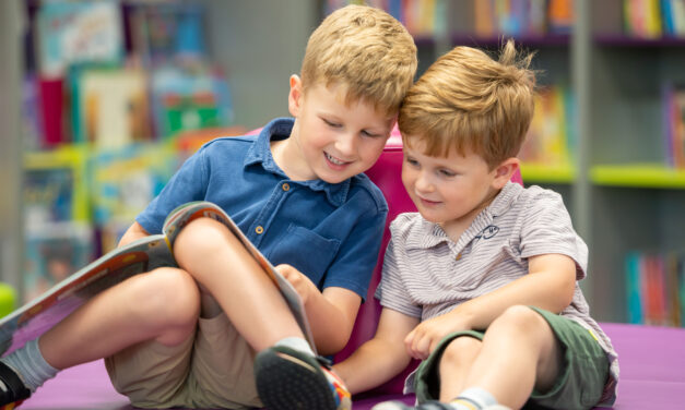 Two young boys reading a book together in a library.