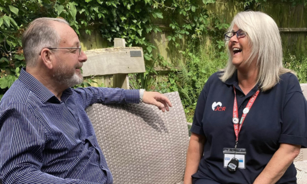 JCR Support worker sits on a garden bench with a client, both looking relaxed and smiling at each other | Support worker jobs in East Sussex