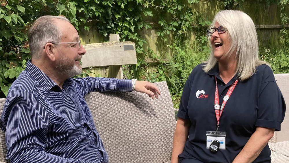 JCR Support worker sits on a garden bench with a client, both looking relaxed and smiling at each other | Support worker jobs in East Sussex