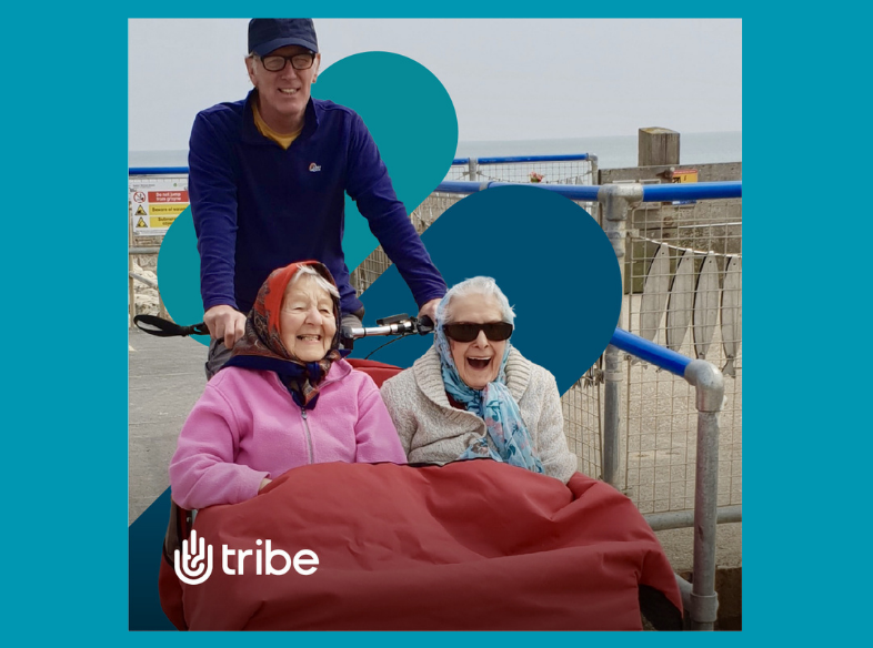 two woman laughing as they're pushed on a wheelchair by a man