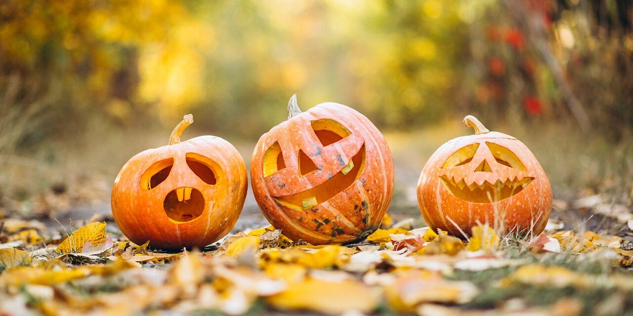 three carved Halloween pumpkins on a path with autumn leaves