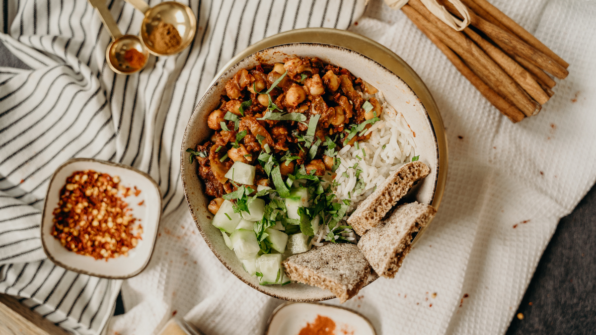 A top down view of a colourful vegetarian meal placed on a table cloth, spices and accessories sit alongside the dish | world vegetarian day recipes