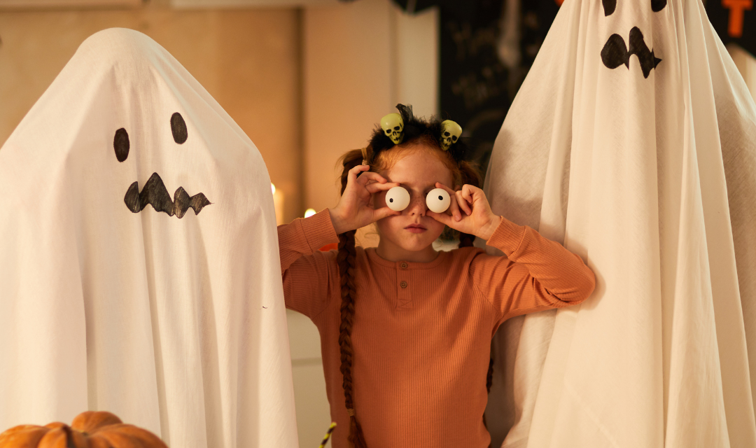 Two people dressed as ghosts with a young girl in between holding up goggly eyes.