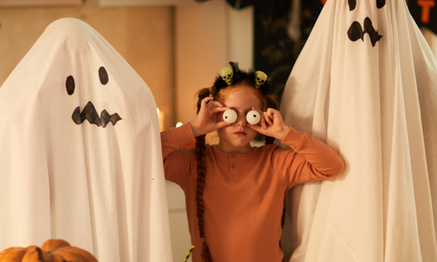 Two people dressed as ghosts with a young girl in between holding up goggly eyes.