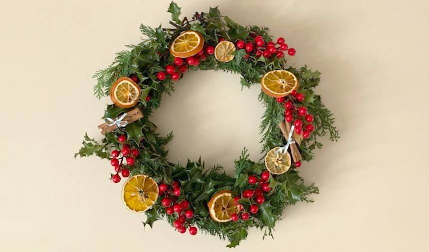 Christmas wreath decorated with confier, holly, ivy, red berries, orange slices and cinnamon sticks.