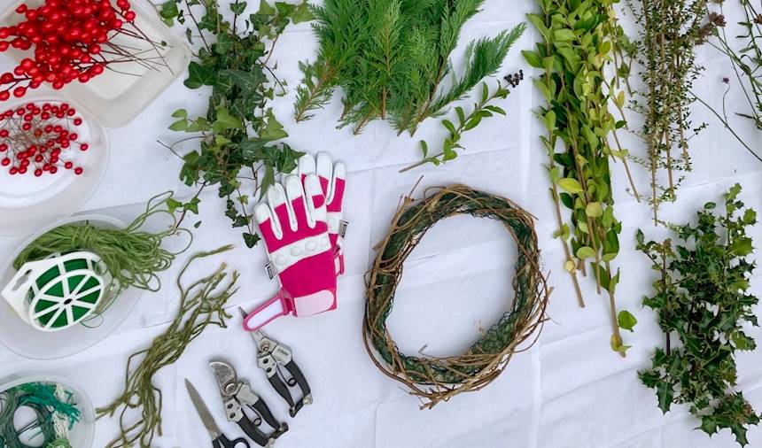 Materials for making a Christmas wreath including evergreen foliage, twigs, garden wire, scissors, secateurs, string, gloves and a wreath base.