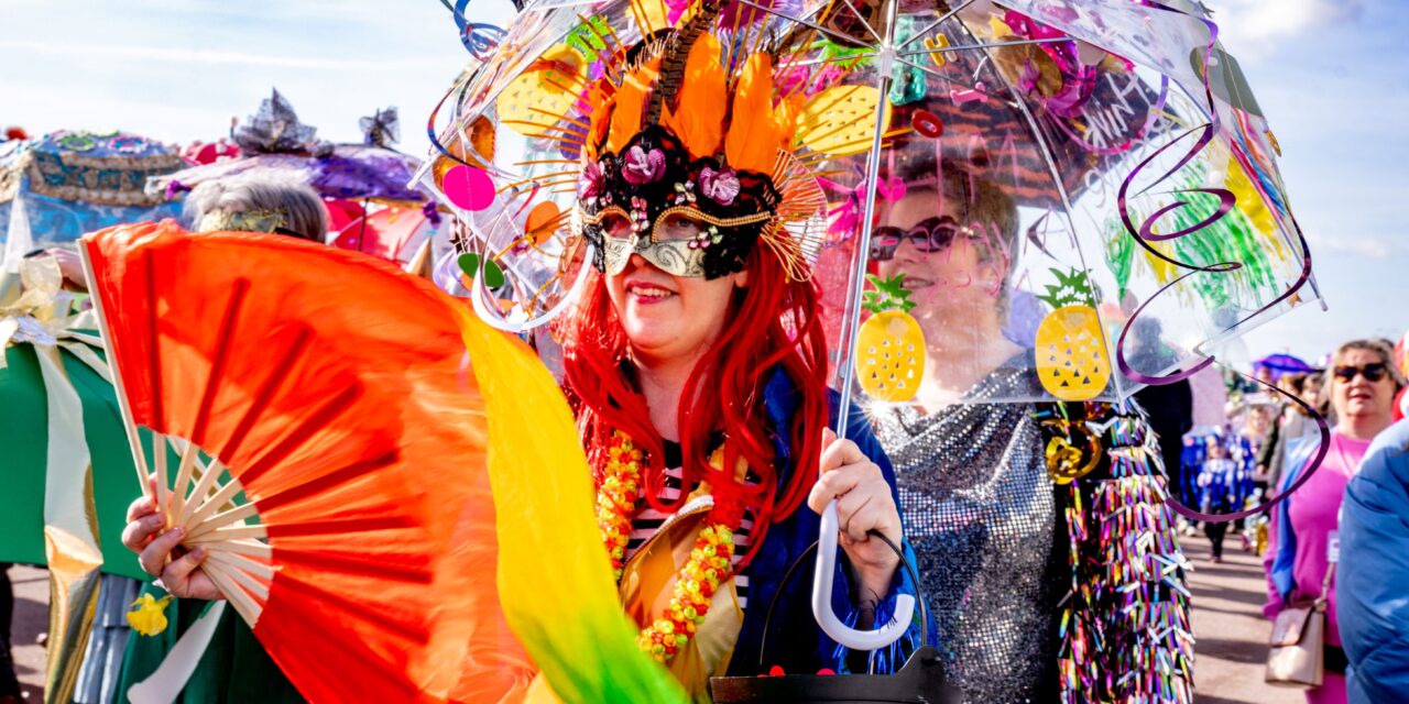 Dressed up women in a parade carrying a decorated umbrella