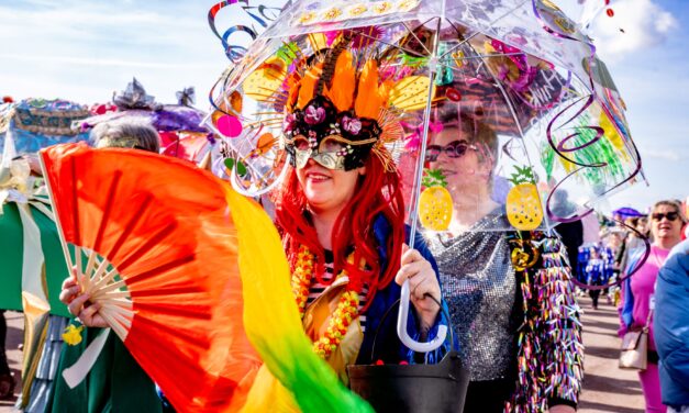 Dressed up women in a parade carrying a decorated umbrella