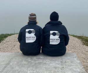 two Beach Head Ambassadors sit on a rock looking out to sea