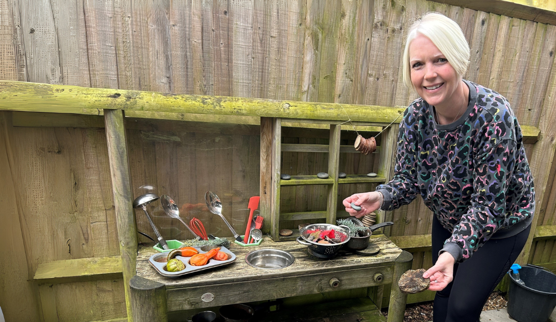 A lady stands next to a a child's mud kitchen