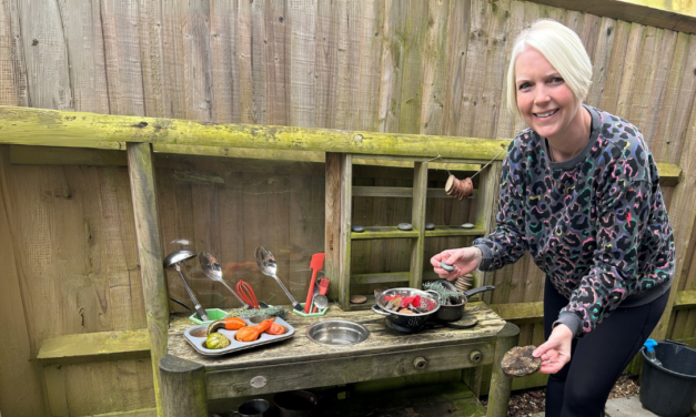 A lady stands next to a a child's mud kitchen