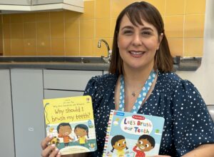 East Sussex oral health trainer Celine Woodthorpe smiles while holding some books for children about brushing their teeth