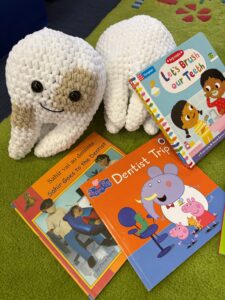 A cute crochet tooth sits next to a selection of children's books about toothbrushing and going to the dentist