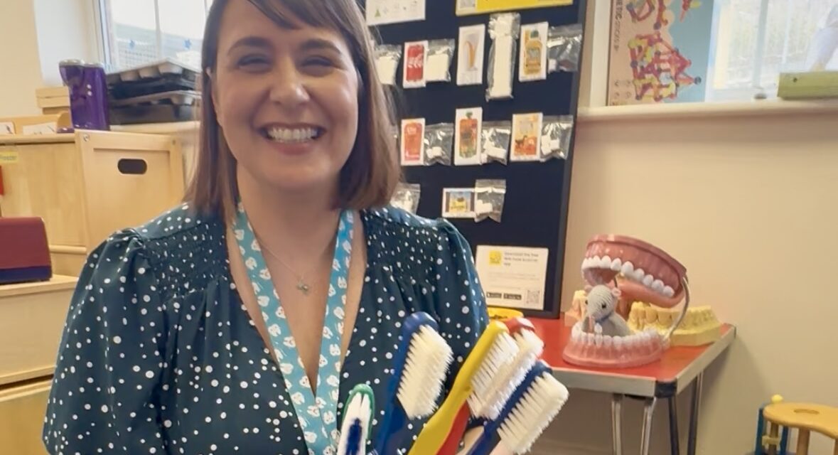 East Sussex oral health trainer Celine Woodthorpe smiles while holding a selection of giant toothbrushes she uses for teaching purposes