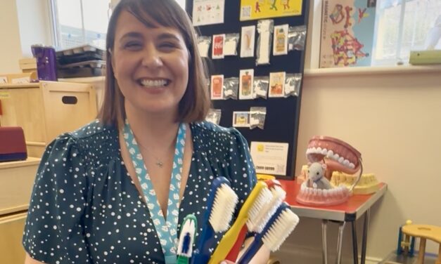 East Sussex oral health trainer Celine Woodthorpe smiles while holding a selection of giant toothbrushes she uses for teaching purposes