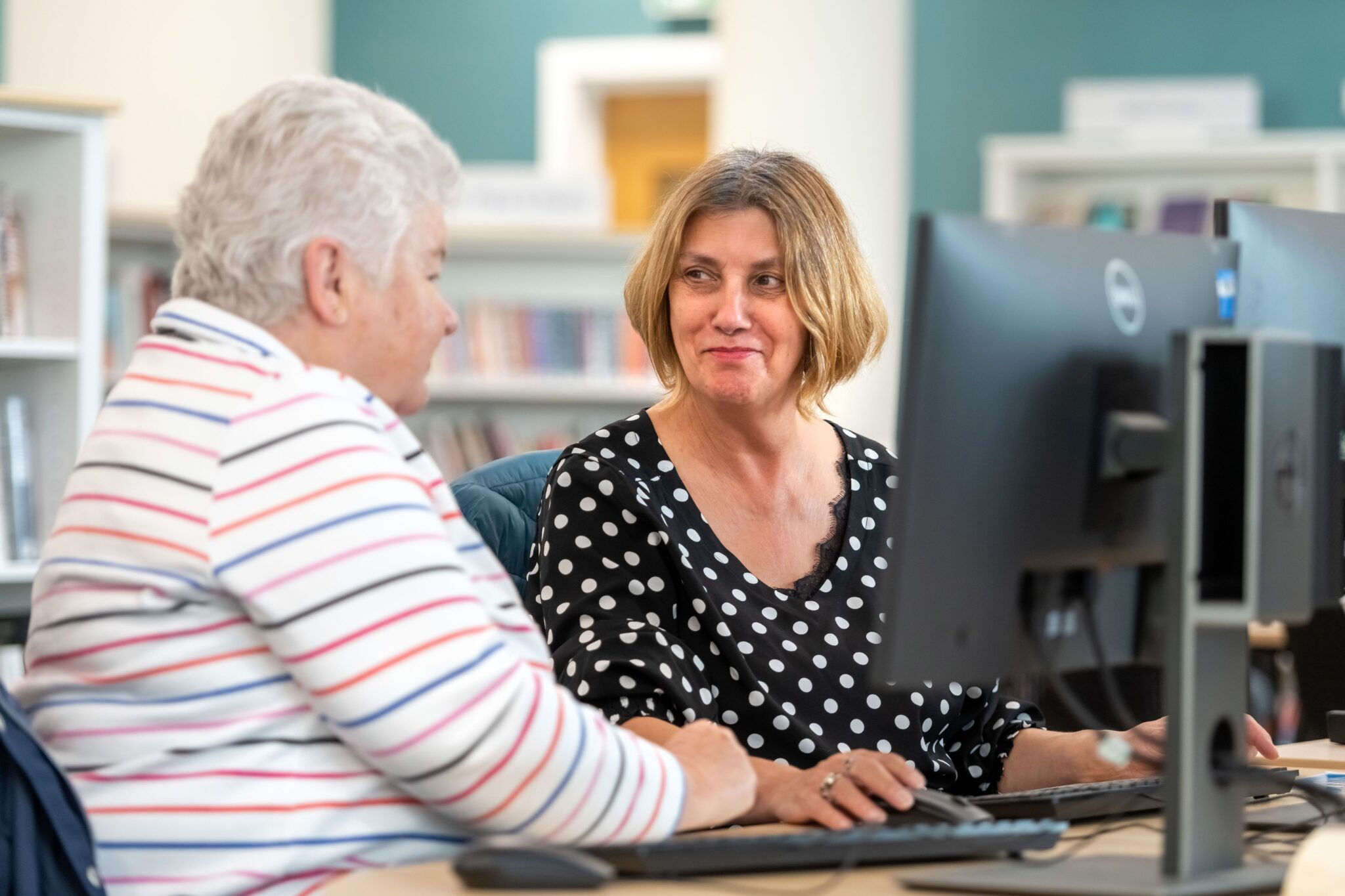 Two ladies sit together in front of a desktop computer in a local East Sussex Library.