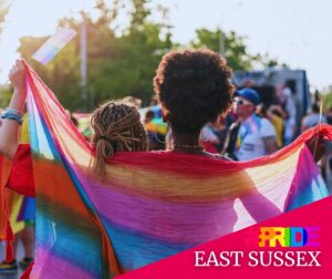 Two people stand side by side with e rainbow flag draped across their shoulders