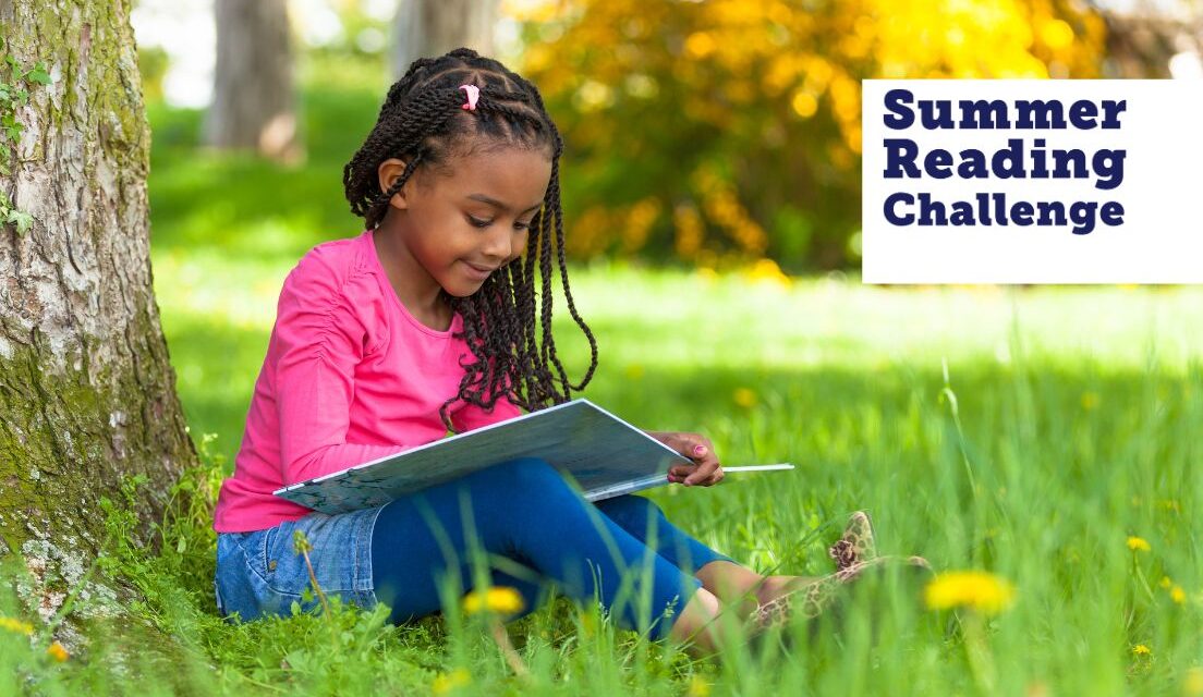 A young girl in a pink top sits on the grass against a tree trunk reading as she takes part in an East Sussex Summer activities for kids: Summer Reading Challenge.