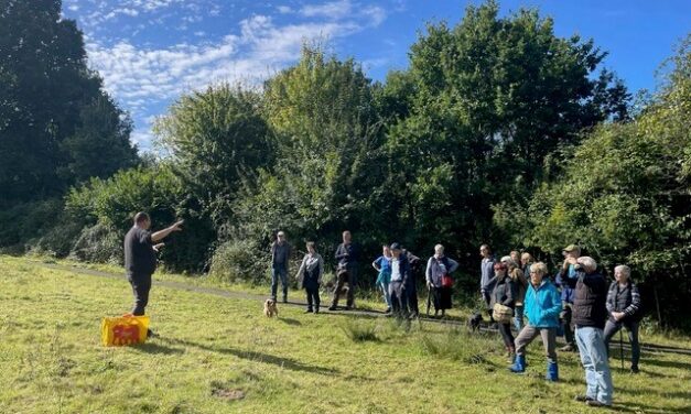 A group of people on a walk standing in a field listening to a guide talking