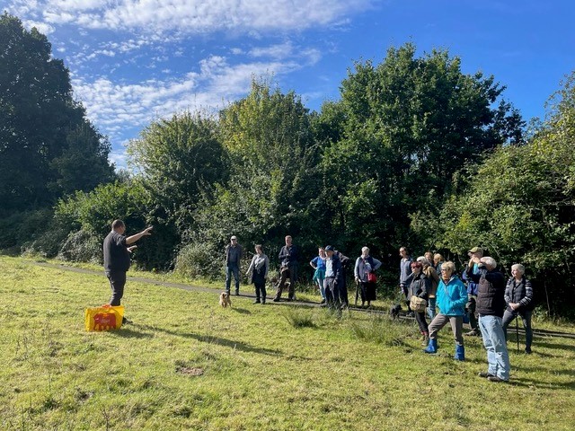 A group of people on a walk standing in a field listening to a guide talking