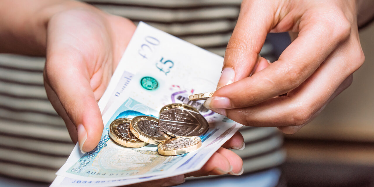 A close up image of hands holding British coins and bank notes.
