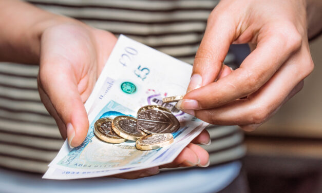 A close up image of hands holding British coins and bank notes.
