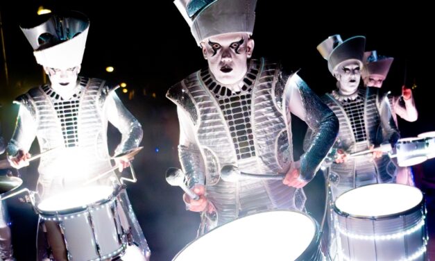 four drummers in silver costumes lit from below