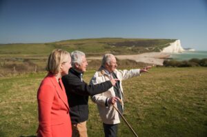 Three people looking out over the South Downs with Cuckmere Haven in the background. The people in the photo are His Majesty the King accompanied by Tony Juniper, Natural England Chair and Emma Reynold, Environment Secretary.