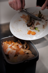 A plate of uneaten food being scrapped into a bin.